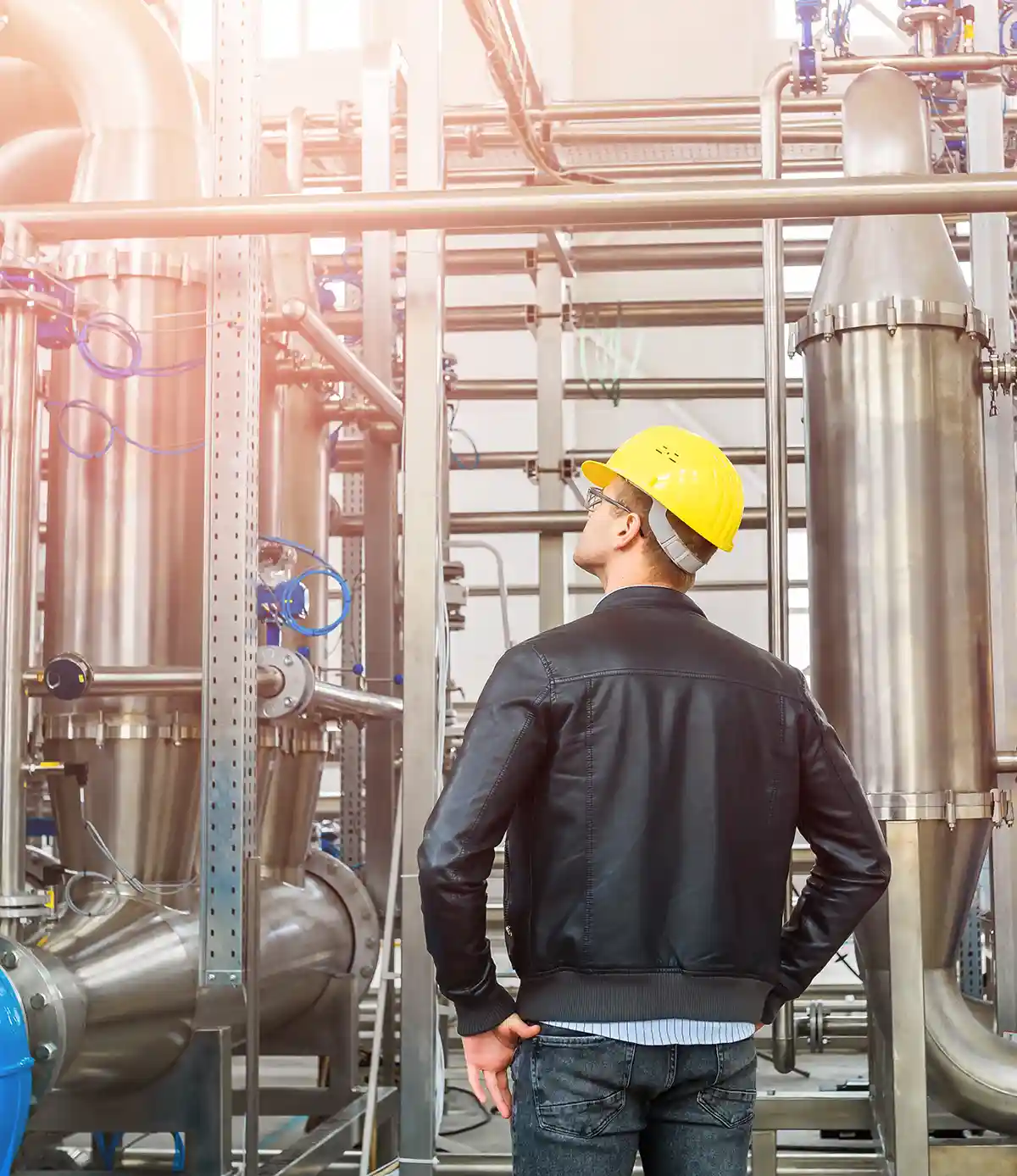 Ein junger Ingenieur mit gelbem Schutzhelm und Jacke prüft in der Fabrik den Betrieb von Rohrleitungen, die zu einer Industrieanlage für die Aufbereitung von kontaminiertem Wasser gehören.